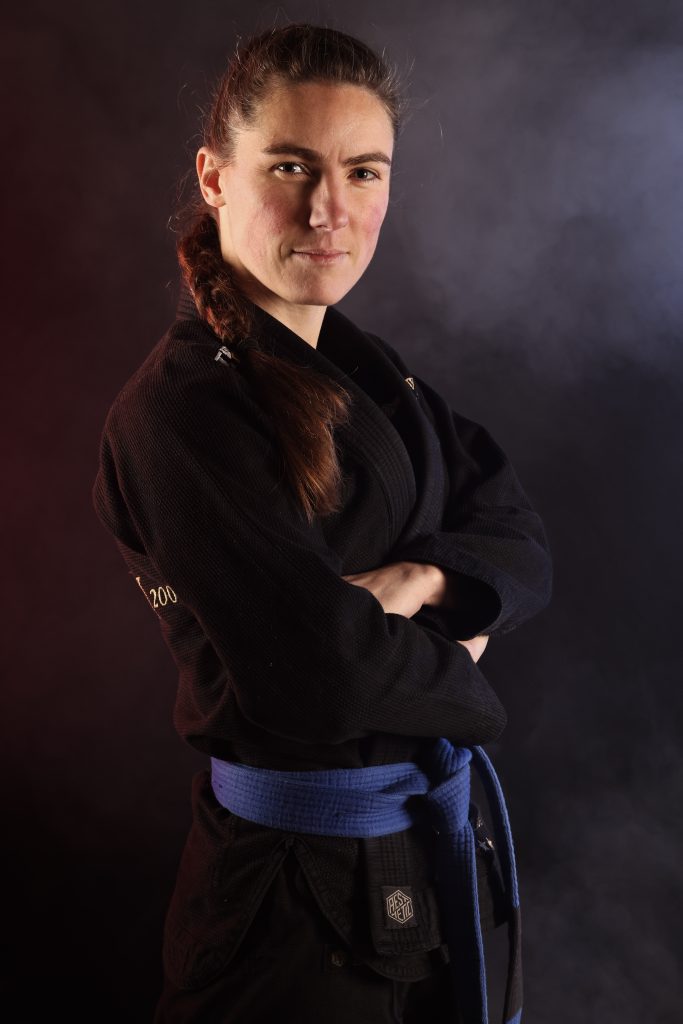 Portrait d’Emily Knight, instructrice de jiu-jitsu brésilien à Vannes, en kimono noir et ceinture violette, photographiée de face, bras croisés, sur fond sombre.